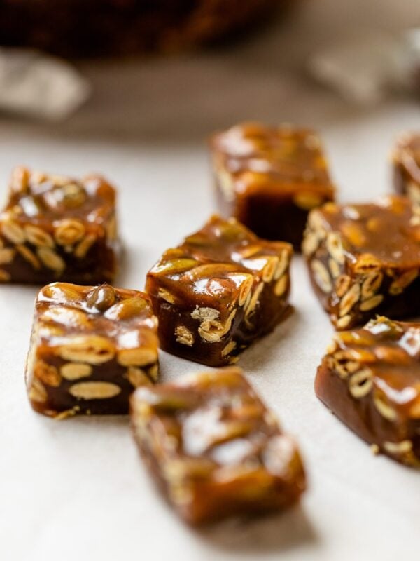 Pumpkin spice caramels sitting on piece of white parchment paper with bowl and wrapped caramels in background