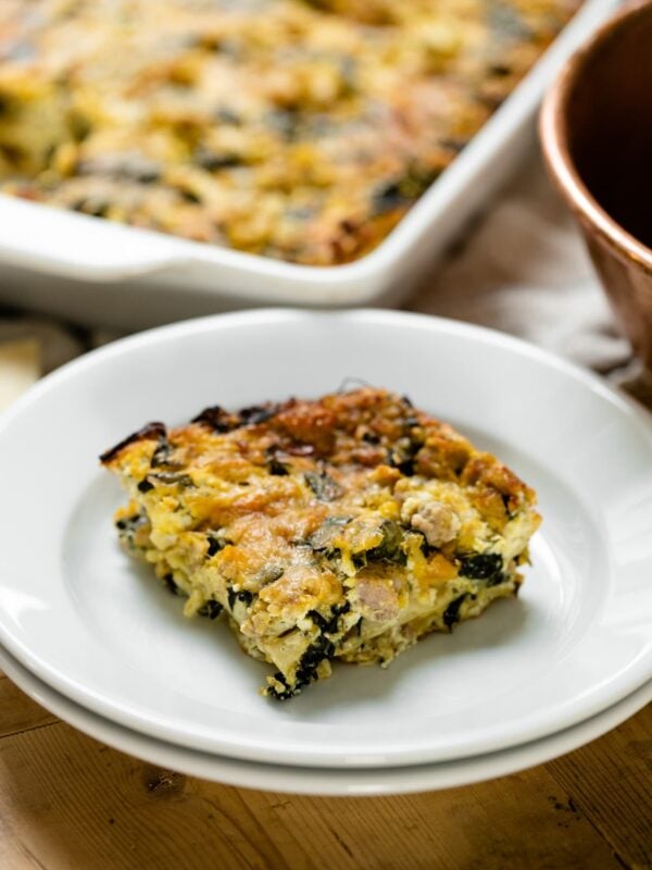 Piece of squash kale lasagna sitting on white plate with rest of lasagna sitting in background
