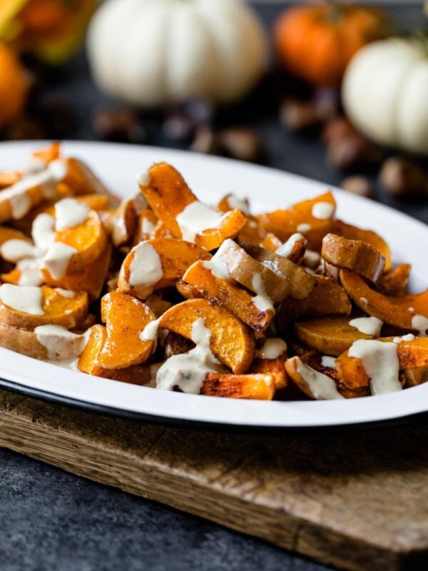 Spiced butternut squash on a white platter sitting on wood board with pumpkins and nuts in background on a gray slate surface