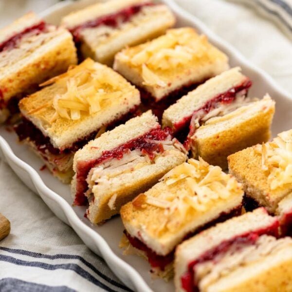 Turkey cranberry croque monsieur sandwiches sitting on white plate with linen napkin underneath on white surface