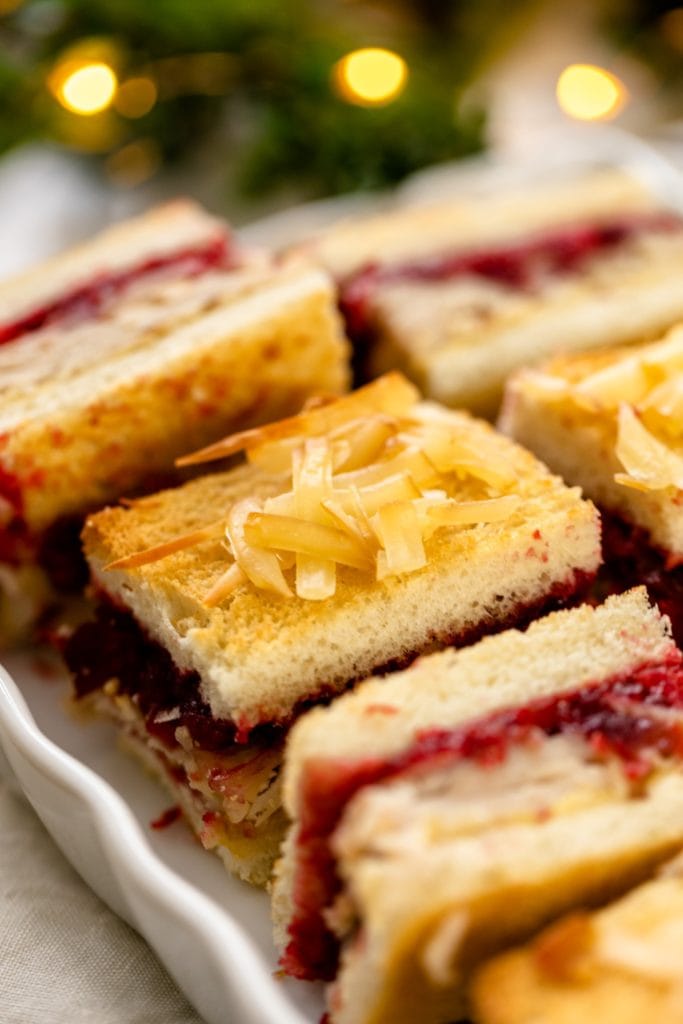 Turkey cranberry croque monsieur sitting on white plate with Christmas lights and greenery in background all on white surface