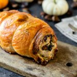 Turkey roulade sitting on wood board with pumpkins and nuts in background with linen napkin and silverware all on a gray slate surface