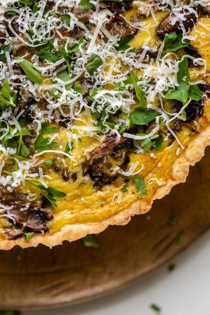 Breakfast quiche topped with parsley and Parmesan cheese sitting on bread board on white sufrace