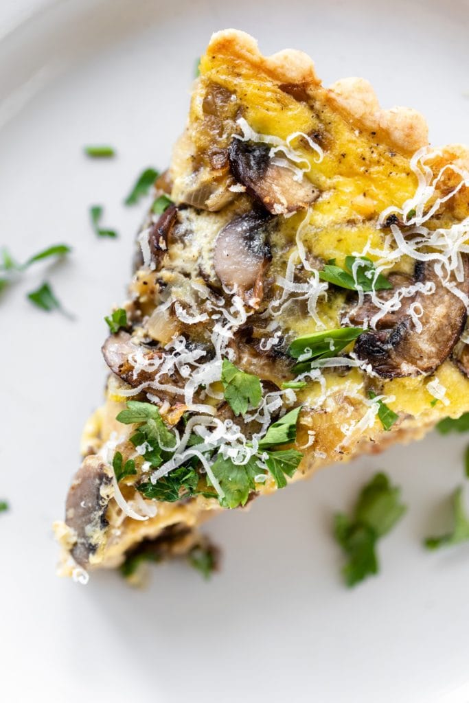 Piece of breakfast quiche topped with parsley and Parmesan cheese sitting on white plate