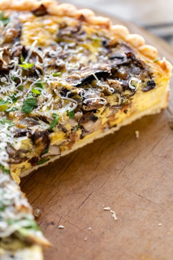 Breakfast quiche topped with parsley and Parmesan cheese sitting on bread board with pieces cut out revealing middle of quiche