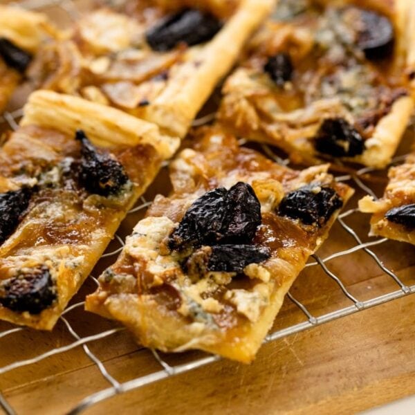 Pieces of caramelized onion tart topped with dried figs and blue cheese sitting on cooling rack on wood board all on white surface