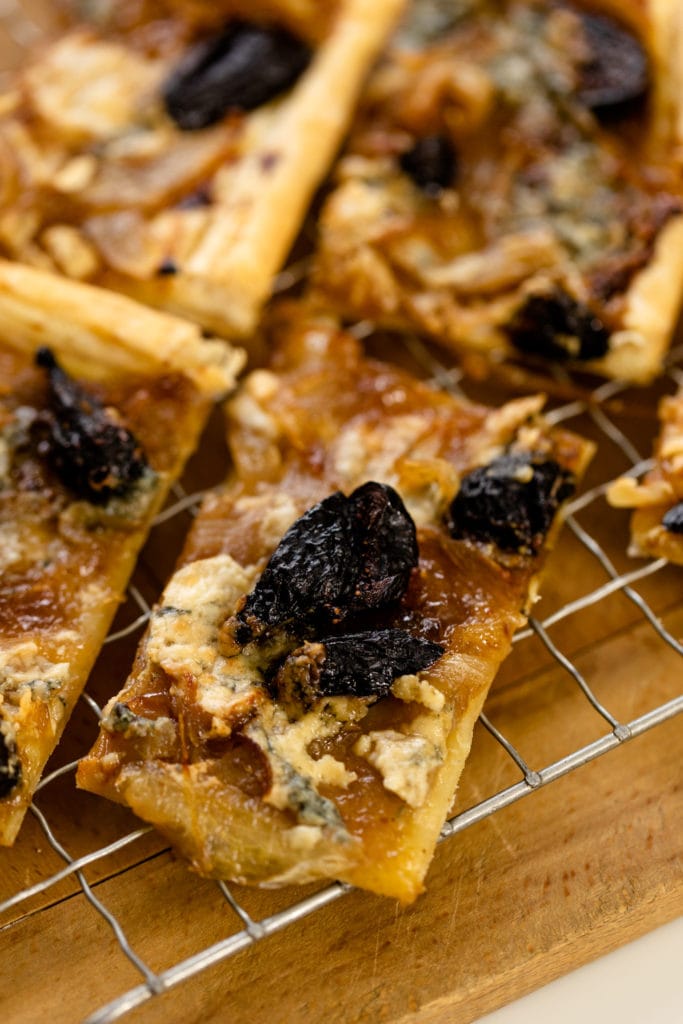 Caramelized onion tart topped with dried figs and blue cheese sitting on wire rack on wood surface