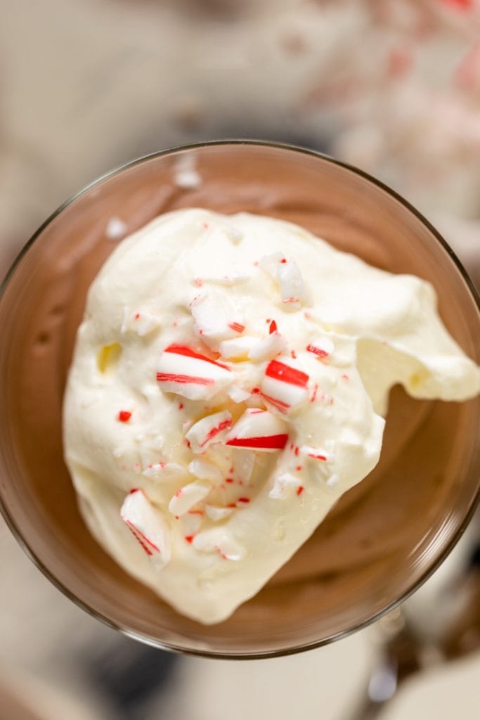 Top down view of chocolate mousse sitting in glass topped with whipped cream and peppermint bits all on a silver tray
