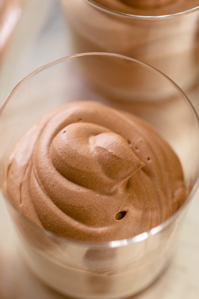 Chocolate mousse sitting in glass container on silver tray with extra glasses of mousse in background