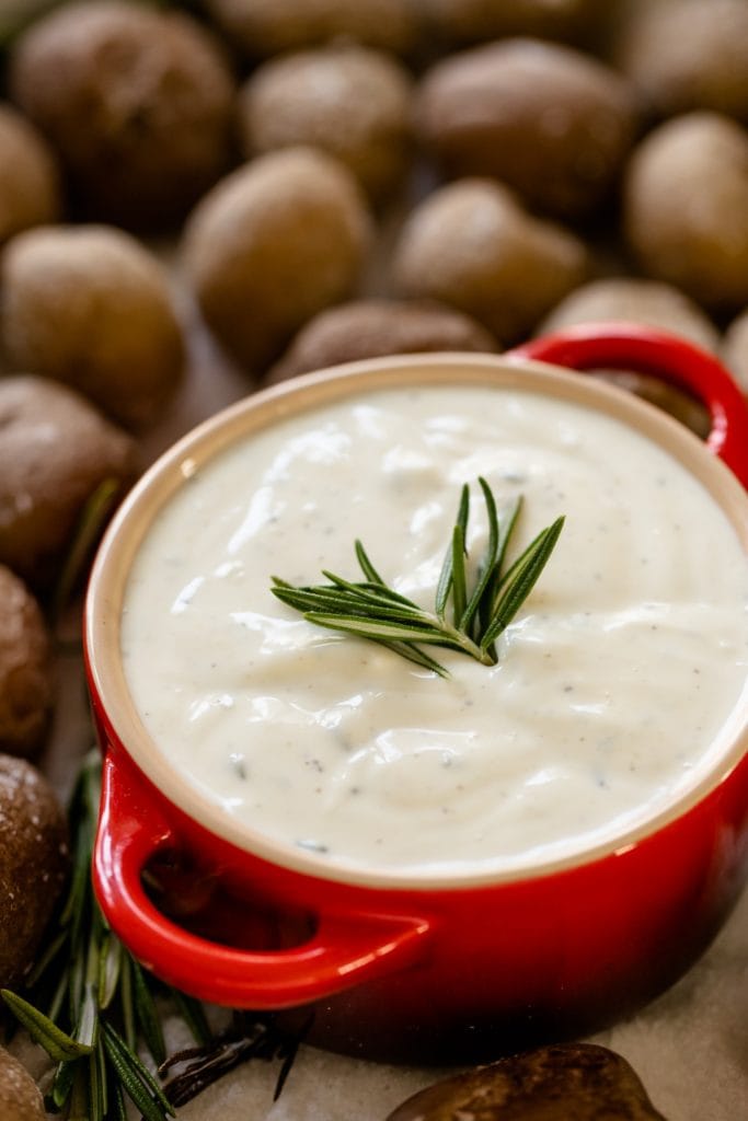 Salt roasted potatoes sitting on bed of salt with red container filled with rosemary ranch dipping sauce