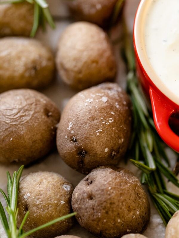 Salt roasted potatoes sitting in a bed of salt with rosemary sprigs place around with red bowl filled with rosemary Ranch dipping sauce