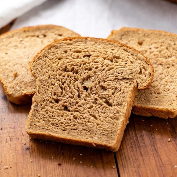 Hearty grain bread sitting on wood board with white parchment underneath with extra loaf in background