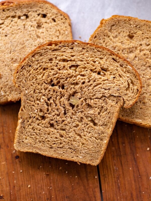 Hearty grain bread sitting on wood board with white piece of parchment in background along with other slices of bread