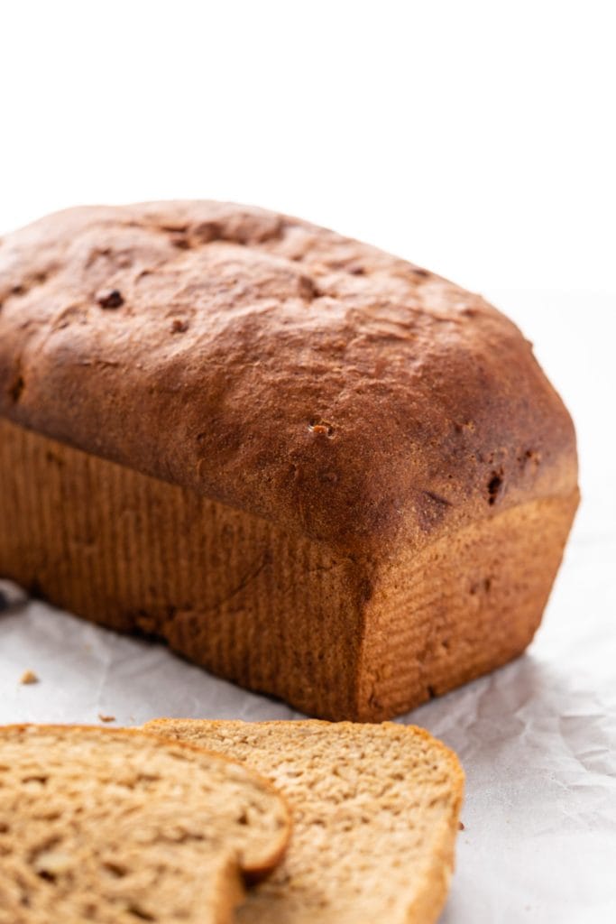 Loaf of hearty grain bread sitting in background on white piece of parchment with extra slices of cut bread in foreground