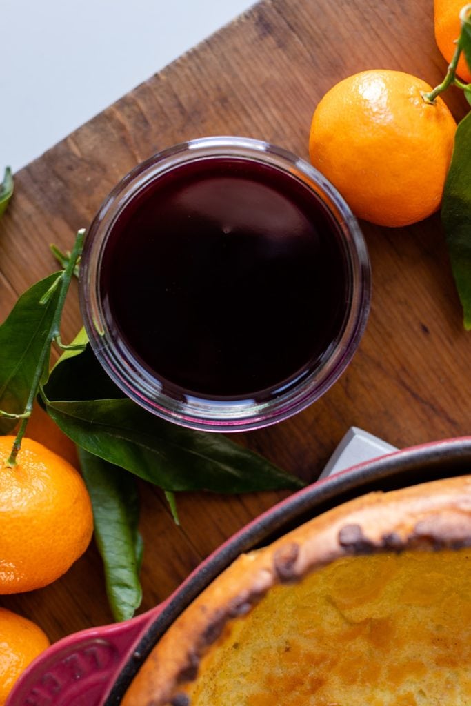 Top down view of berry coulis sauce sitting in glass jar surrounded by oranges on a wood surface