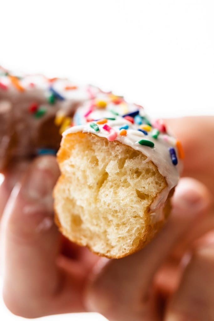 Close up view of inside of glazed homemade donut with white frosting and sprinkles on top being held by hand