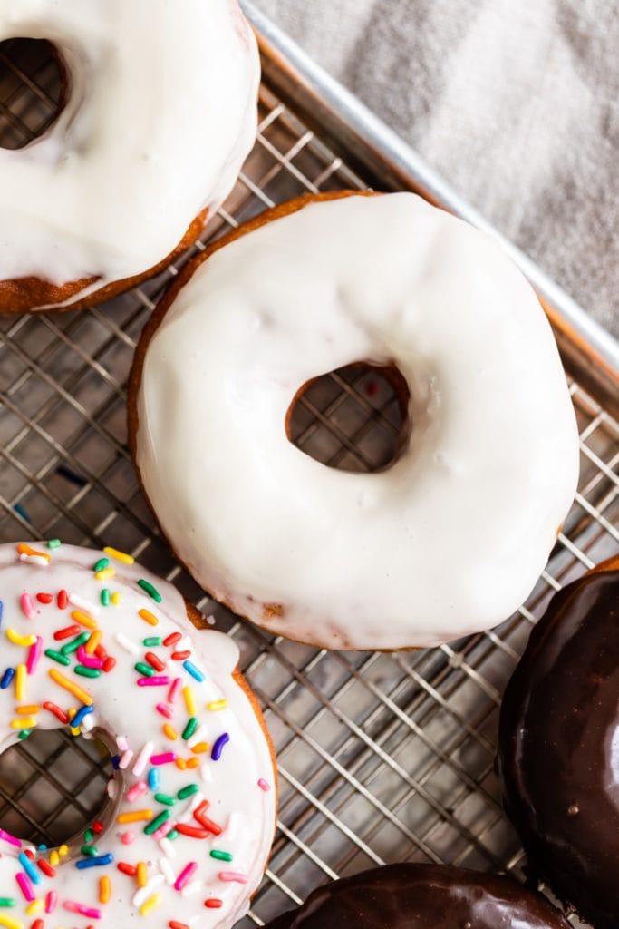 Top down view of homemade yeast donut topped with vanilla glaze sitting on wire cooling rack with linen towel underneath