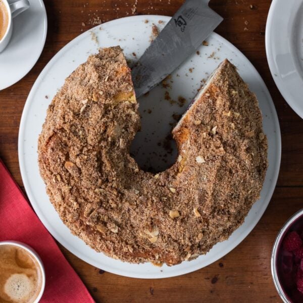 Top down view of raspberry blood orange coffee cake with slices or cake removed with extra raspberries on wood board
