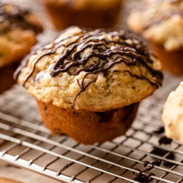 Banana chocolate chunk muffins sitting on wire cooling rack on wood board with piece of parchment underneath