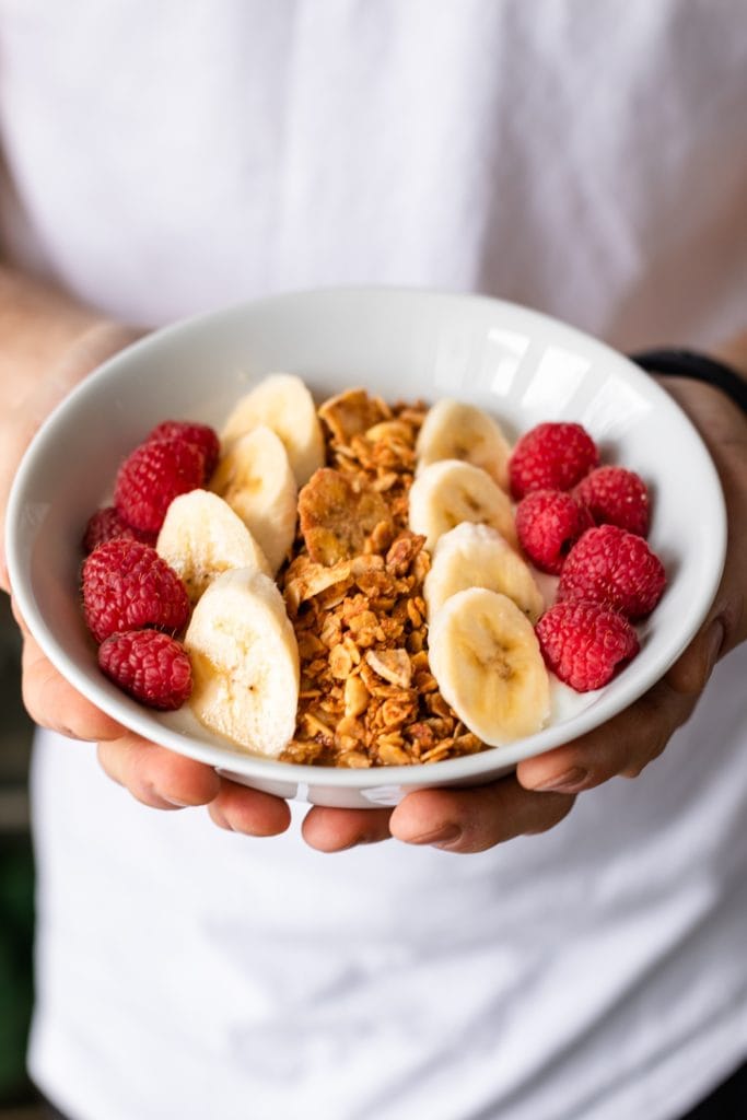 Hands holding bowl of peanut butter granola with white shirt and black pants in background