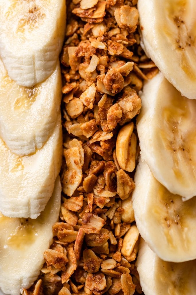 Close up view of homemade peanut butter granola nestled in between slices of banana