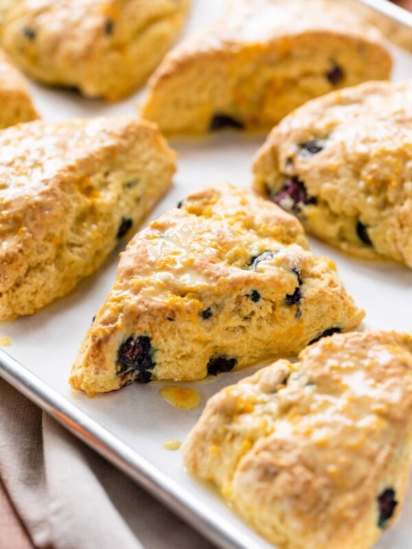 Orange and blueberry Irish soda bread scones topped with glaze sitting on parchment-lined baking sheet