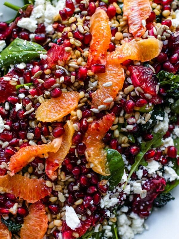 Top down view of blood orange and wheat berry salad sitting on white platter sprinkled with pomegranate arils and feta cheese