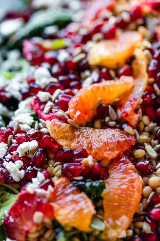Close up view of blood oranges situated on top of salad greens sprinkled with sunflower seeds and feta cheese