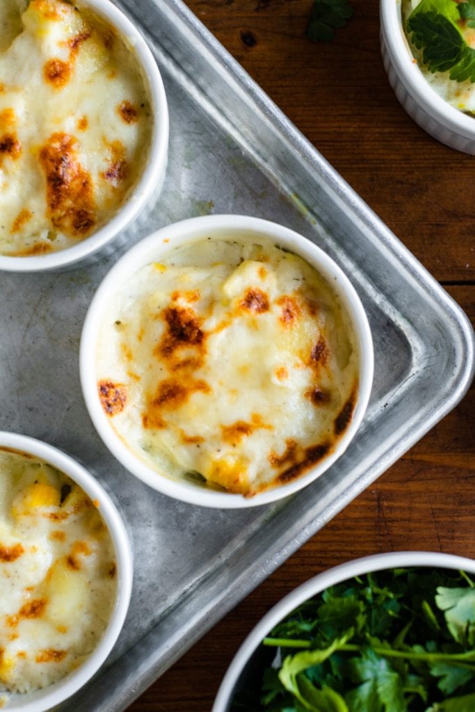 Top down view of egg casserole in individual ramekin contains sitting on metal baking tray with bowl of parsley to the side all on wood surface