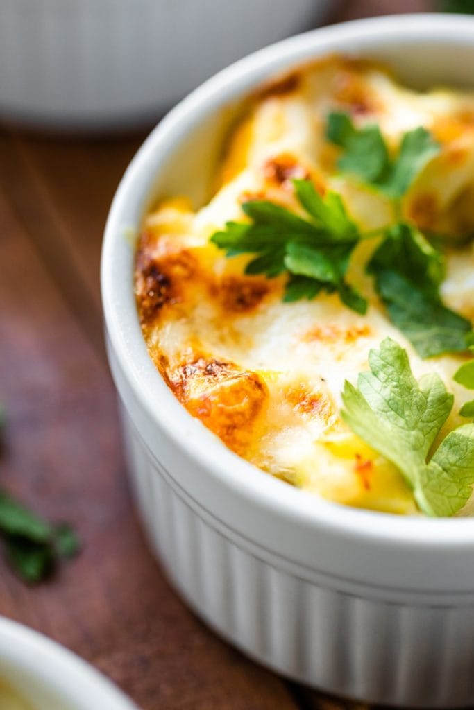 Close up view of brown bits of egg casserole baked in individual ramekin and topped with parsley on a wood surface