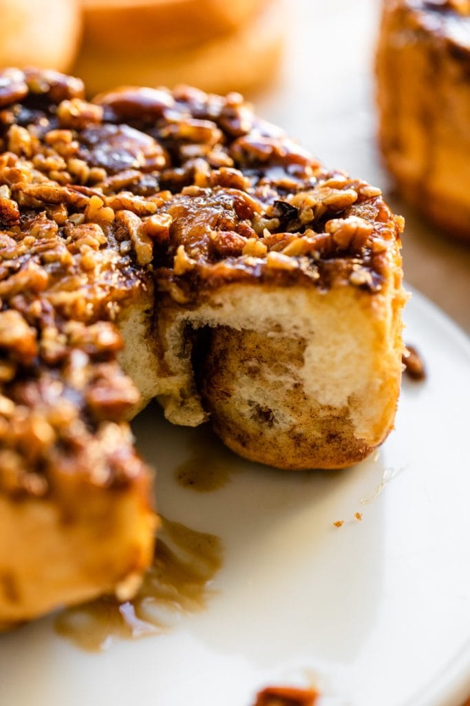 Inside view of sticky caramel rolls with one piece missing topped with chopped pecans and caramel sauce