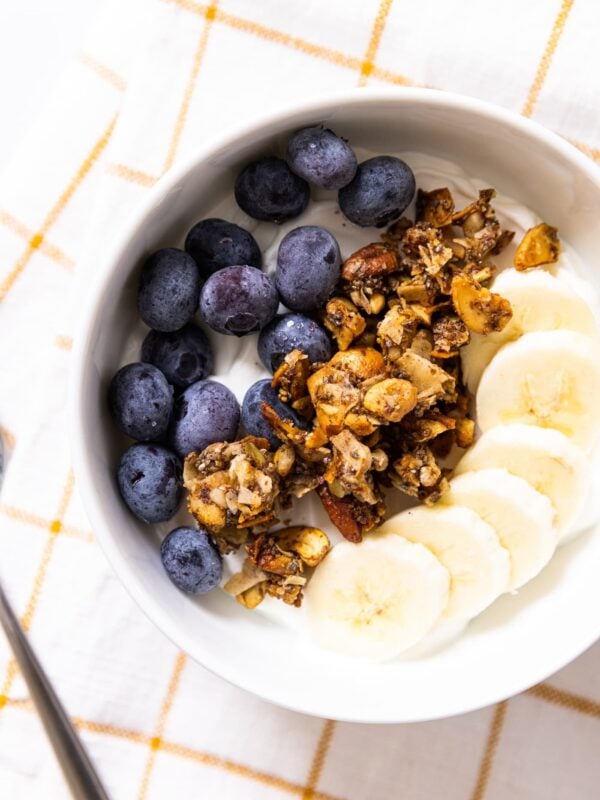 Top down view of white bowl filled with blueberries and bananas and grain-free granola sprinkled on top of yogurt