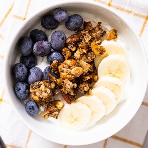 Top down view of white bowl filled with yogurt with blueberries and bananas and grain-free granola piled on top all with striped yellow towel underneath