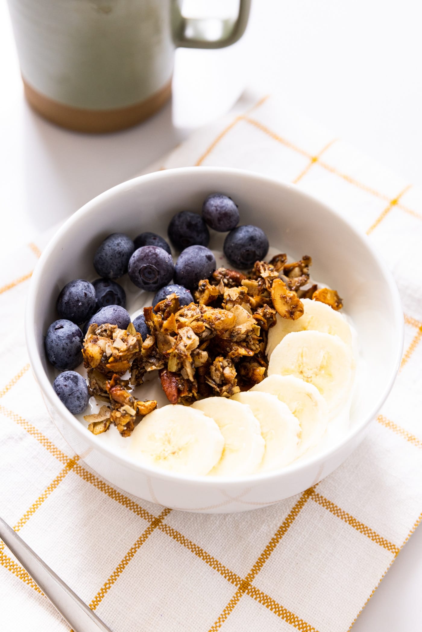 White bowl filled with yogurt and topped with blueberries and grain-free granola.