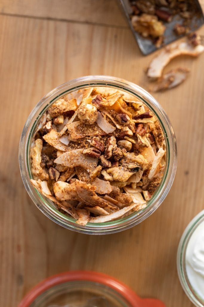 Top down view of grain-free granola in glass container sitting on wood surface with extra granola sitting on side