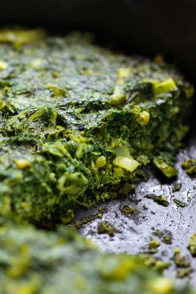 Close up view of inside of herb omelet with leek protruding all in cash iron pan