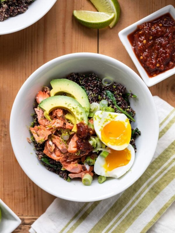 Top down view of bed of quinoa topped with salmon, avocado, and a sliced egg with linen towel underneath all on wood surface
