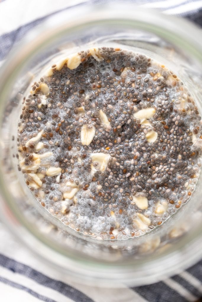 Top down view of chia seeds sitting in oatmeal in glass container with striped linen underneath