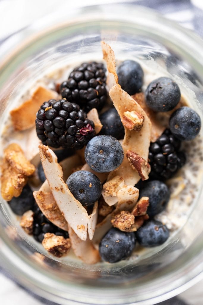 Blueberries, blackberries, and granola sitting on top of container of overnight oats