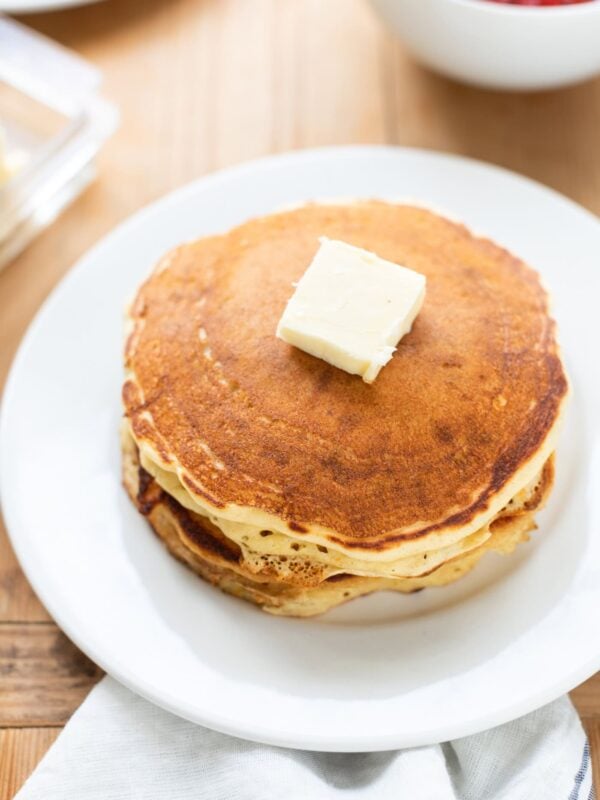 White plate with stack of buttermilk pancakes with pat of butter on top.