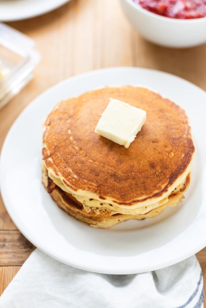 White plate with stack of buttermilk pancakes with pat of butter on top.