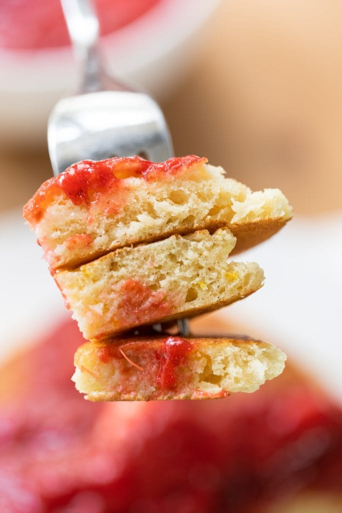 Slice of three buttermilk pancakes on a fork being held in front of plate full of rest of pancakes