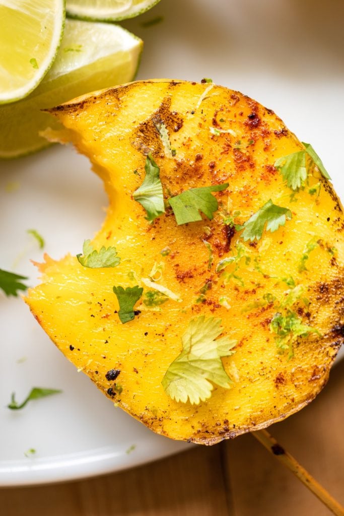 Mango sitting on white serving platter with bite taken out and topped with cilantro and spices