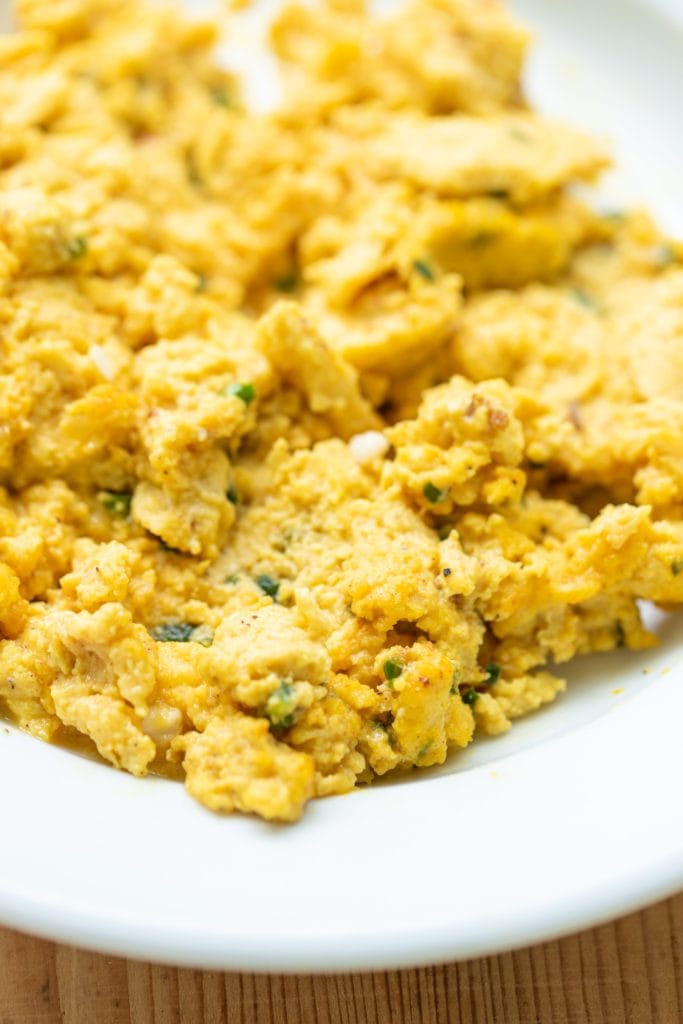 White bowl filled with yellow eggs dotted with pieces of jalapeno