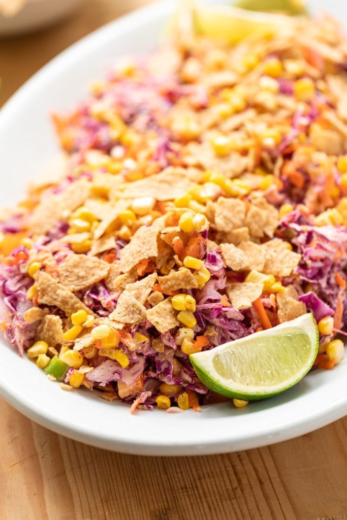 Tex-Mex coleslaw served on white serving platter topped with crushed tortilla chips and lime wedge all on wood surface