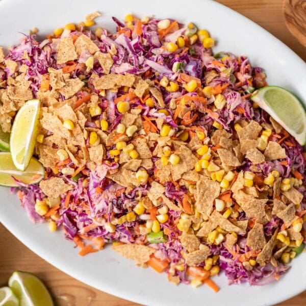 Top down view of Tex-Mex coleslaw served on white plate with lime wedges and tortilla chips crumbled on top all on wood surface