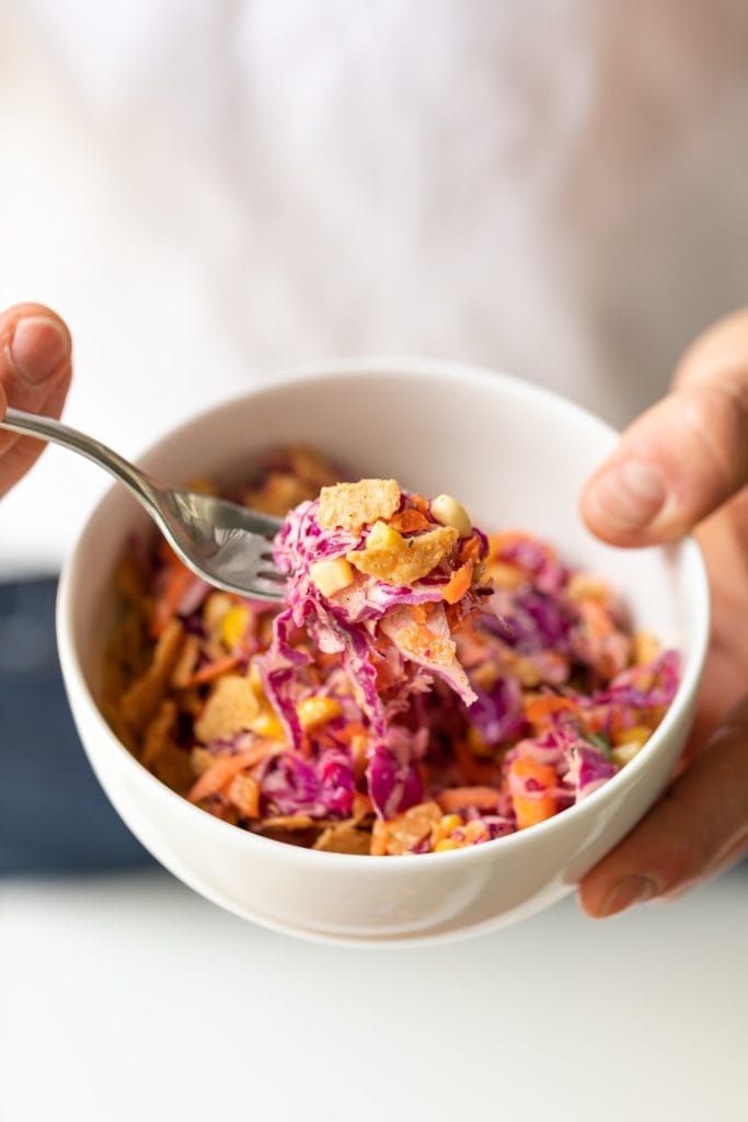 Two hands holding bowl filled with coleslaw made from red cabbage with fork holding bite
