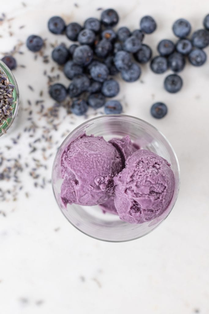 Top down view of purple blueberry lavender ice cream with blueberries and dried lavender sitting on marble surface