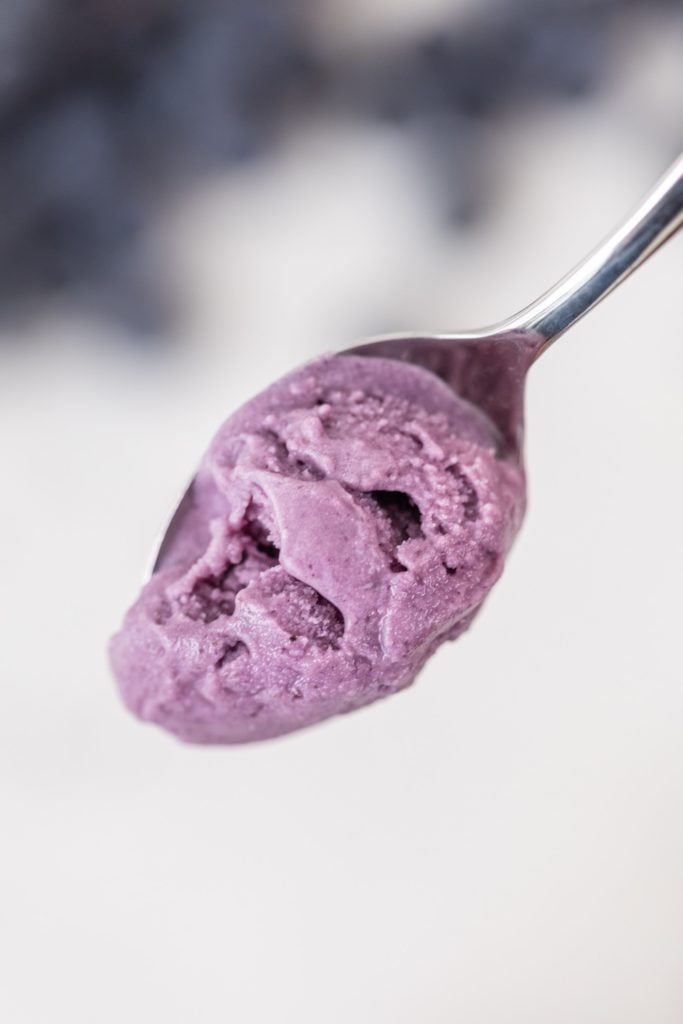 Spoon full of blueberry lavender ice cream with blurry blueberries on marble surface in background