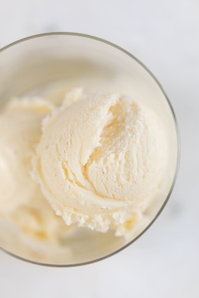 Top down view of orange sage ice cream sitting in glass container on marble surface